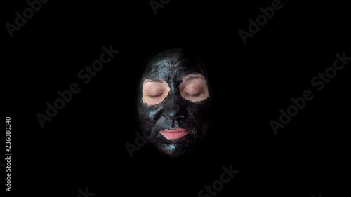 Young woman. Black cosmetic mask on the face. Black background. Close-up portrait. A towel on your head. Wearing a housecoat. Design element.