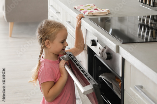 Little girl opening oven while baking in kitchen