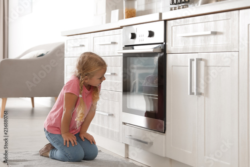 Little girl sitting near oven in kitchen