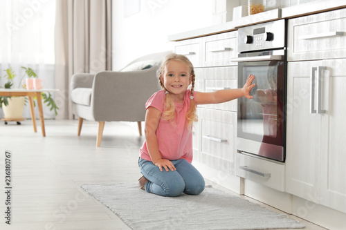 Little girl sitting near oven in kitchen. Space for text