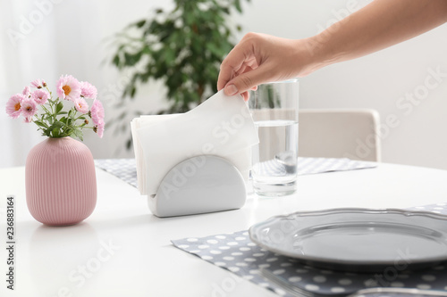 Woman taking paper tissue from ceramic napkin holder on served table