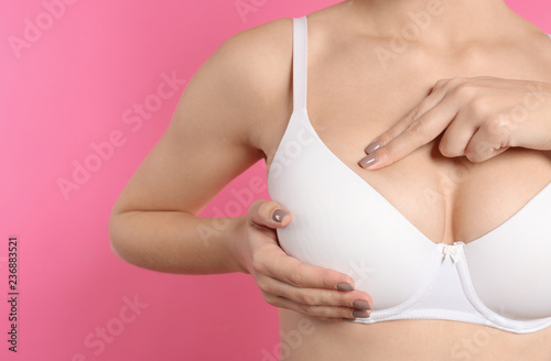 Woman checking her breast on color background, closeup