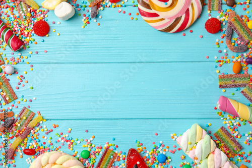 Flat lay composition with different yummy candies and space for text on color wooden background