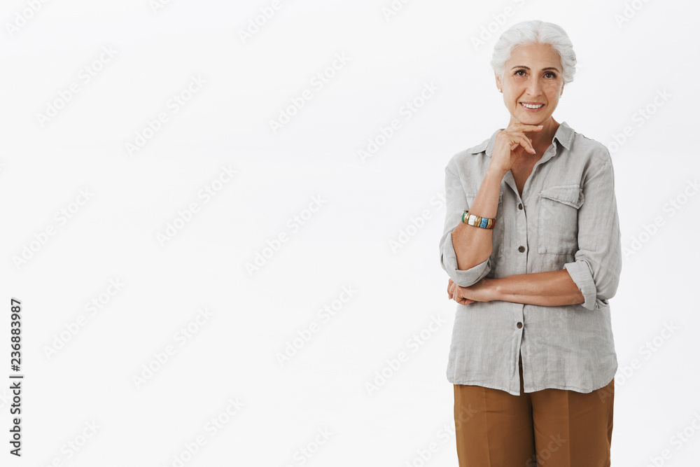 Portrait of charming beautiful old woman with grey combed hair holding hand on chin and gazing interested at camera hearing curious and intriguing promotion deciding how invest money Portrait of charming beautiful old woman with grey combed hair holding hand on chin and gazing interested at camera hearing curious and intriguing promotion deciding how invest money
