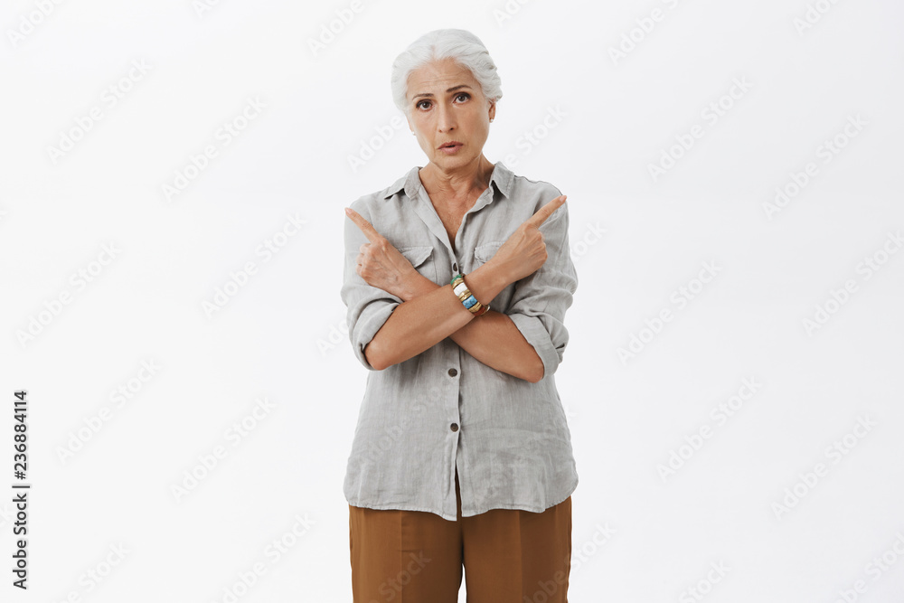 Old woman cannot decide which way better. Portrait of confused unsure granny with grey hair in casual shirt crossing arms on chest pointing left and right having trouble in making decision or choice Old woman cannot decide which way better. Portrait of confused unsure granny with grey hair in casual shirt crossing arms on chest pointing left and right having trouble in making decision or choice
