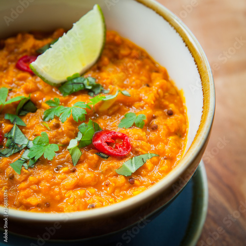 Indian Lentil Dal with red lentils, tomatoes, carrot, lime, cocnut cream, turmeric, curry powder, cumin seeds and mustard seeds. decorated with fresh cilantro, chilli and plant based coconut cream. photo