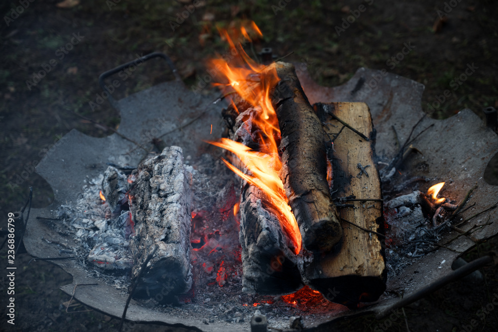 old fire bowl with burning wood logs warms up at an outdoor party in the cold night, copy space, selected focus, narrow depth of field old fire bowl with burning wood logs warms up at an outdoor party in the cold night, copy space, selected focus, narrow depth of field