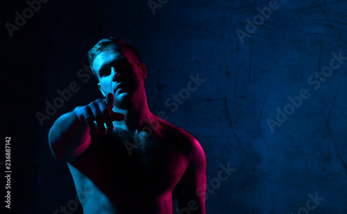 Neon light portrait of sexy man muscular body and white t-shirt pointing hands finger at the corner