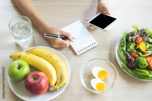 Dieting and calories control for wellness. Woman using smartphone calculate calories of food in breakfast during dieting for lose weight program and take notes. photo