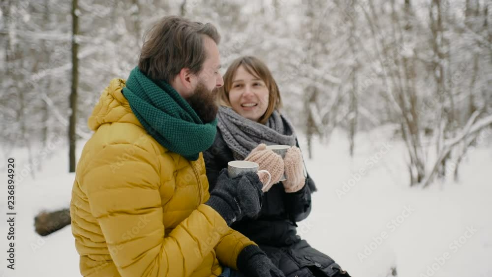A boy and a girl, dressed in warm winter clothes, enjoy each other's presence in a snowy winter park, warming each other, and drinking a hot drink. 4к. A boy and a girl, dressed in warm winter clothes, enjoy each other's presence in a snowy winter park, warming each other, and drinking a hot drink. 4к.