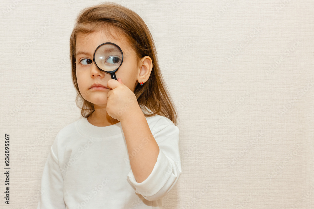 Little girl child looking through a magnifying glass on beige background. Children's curiosity. girl is playing doctor Little girl child looking through a magnifying glass on beige background. Children's curiosity. girl is playing doctor