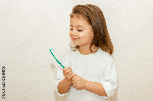 Little baby girl hold and look at toothbrush in hand. Toddler learning to clean tooths. Healthy lifestyle, not afraid of dentist office. Health care, dental hygiene.
