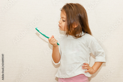 Little baby girl hold and look at toothbrush in hand. Toddler learning to clean tooths. Healthy lifestyle, not afraid of dentist office. Health care, dental hygiene.