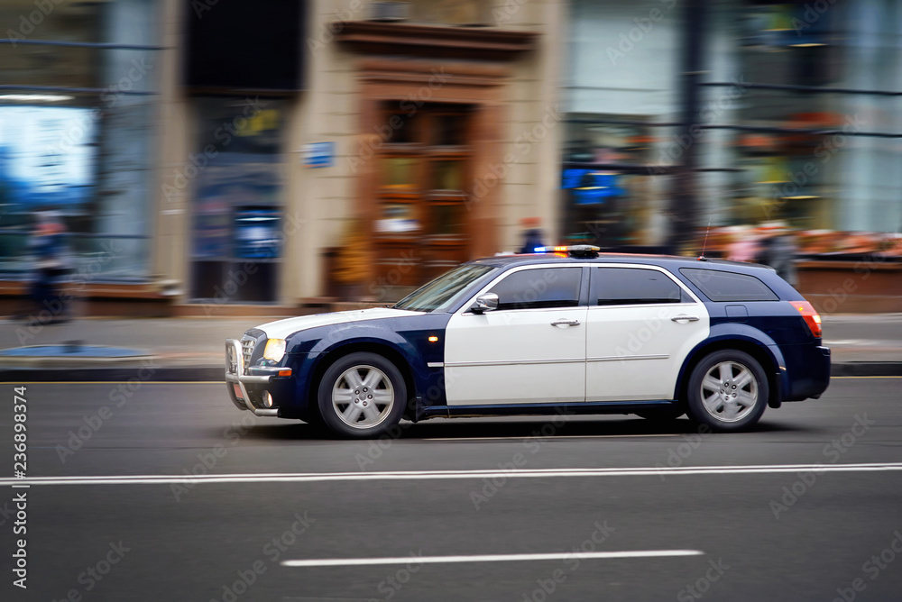 Modern police car chases the offender at high speed with the siren and lights in the city. Policemen serve on city roads. Rush to the scene. Prevention of crime. Elite Police Unit.Charged car racing