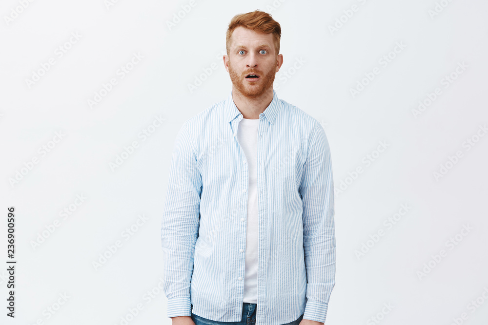 Redhead man standing like zombie in stunned, staring amazed at camera, dropping jaw, being shocked and amazed to bottom of heart, posing over gray background in casual blue shirt Redhead man standing like zombie in stunned, staring amazed at camera, dropping jaw, being shocked and amazed to bottom of heart, posing over gray background in casual blue shirt