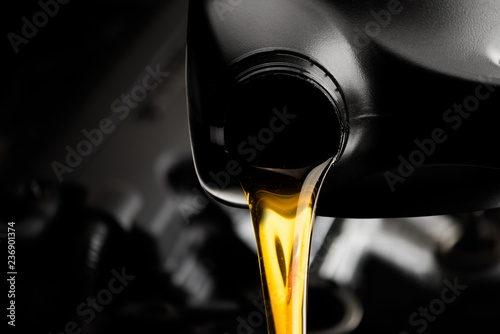 Pouring oil motor car lubricant from black bottle on engine background , service oil change auto repair shop