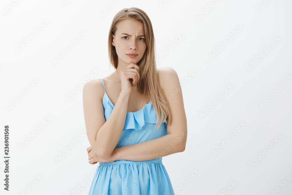 Hmm girl suspect something wrong. Portrait of serious-looking concerned and thoughtful good-looking blond woman in blue dress frowning as thinking holding hand on chin, being doubtful or suspicious Hmm girl suspect something wrong. Portrait of serious-looking concerned and thoughtful good-looking blond woman in blue dress frowning as thinking holding hand on chin, being doubtful or suspicious