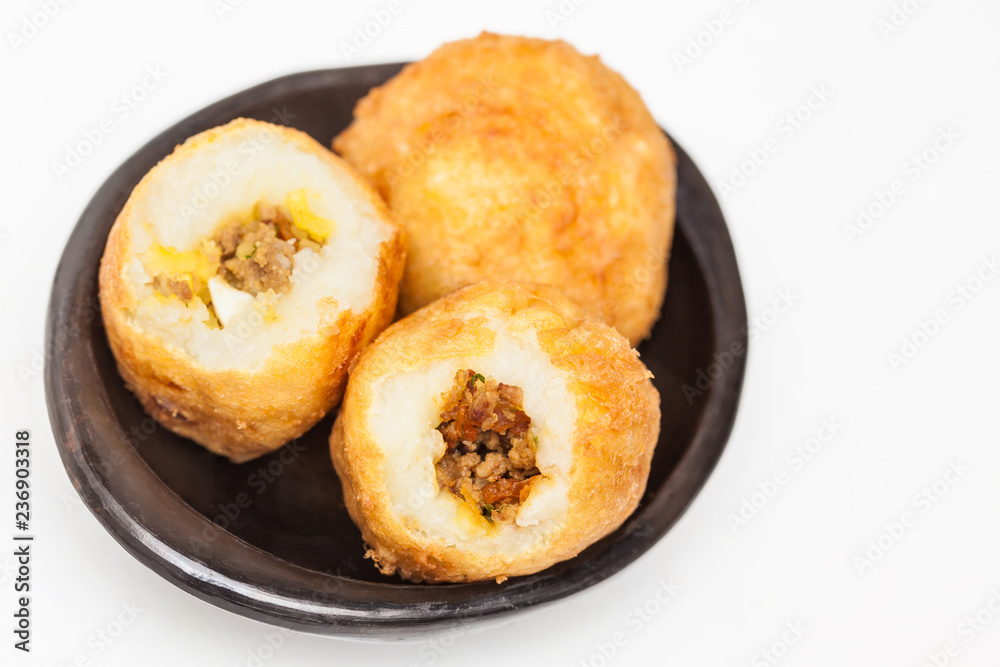 Preparation steps of traditional Colombian dish called stuffed potatoes : Ready stuffed potatoes served in a black ceramic dish isolated on white background