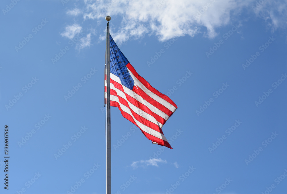 Backlit American flag on flagpole on a windy day against blue sky with light clouds