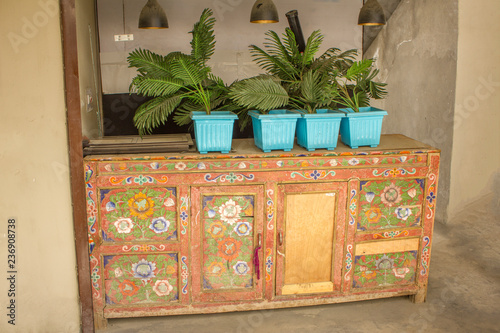 An old multicolored wooden table with doors and famous plants standing on it in blue pots.