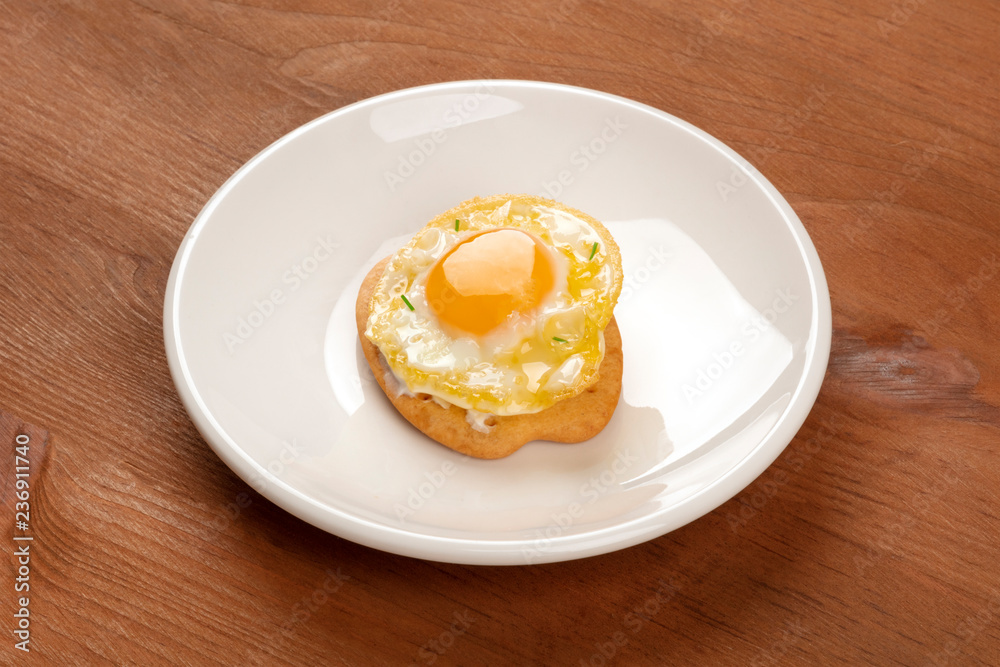 A photo of a quail egg, fried sunny side up, on a cracker, on a dark rustic wooden background