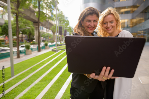 Portrait of two happy businesswoman using laptop computer together outdoors © Ranta Images