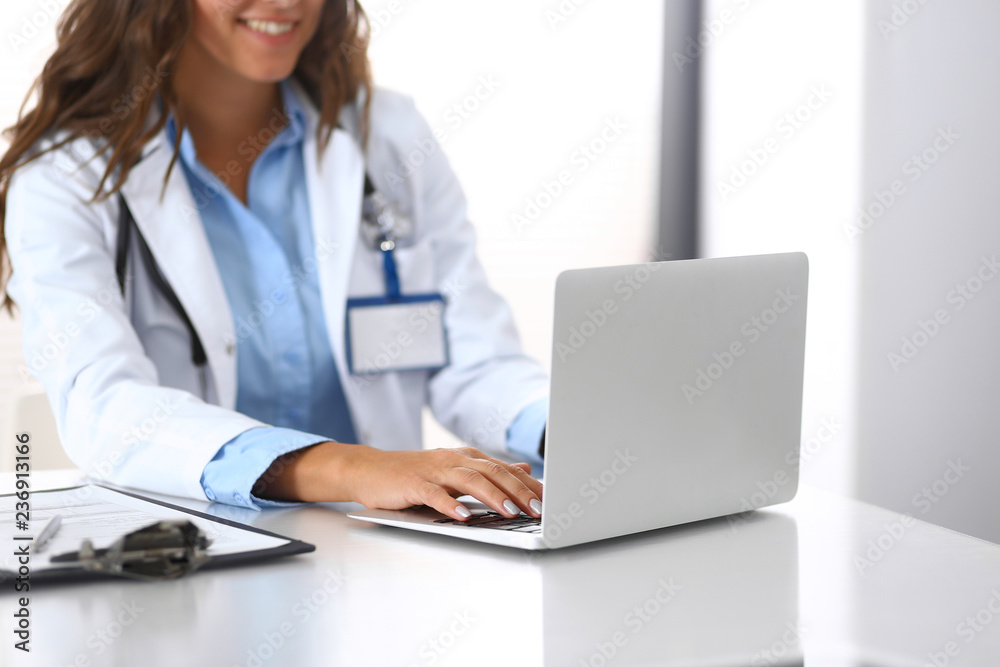 Unknown doctor woman typing on laptop computer while sitting at the desk in hospital office. close-up of hands. Physician at work. Medicine and health care concept Unknown doctor woman typing on laptop computer while sitting at the desk in hospital office. close-up of hands. Physician at work. Medicine and health care concept
