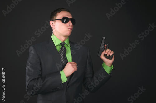 Arrogant security agent is posing with a gun in hand like a super spy isolated on black background. photo