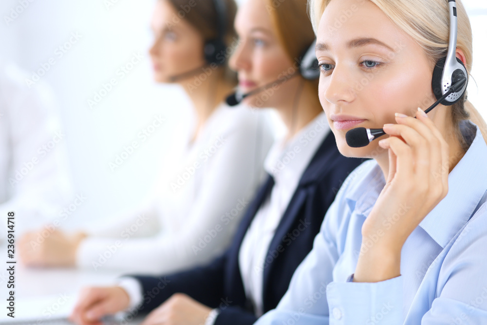 Call center. Group of operators at work. Focus at blonde business woman in headset Call center. Group of operators at work. Focus at blonde business woman in headset