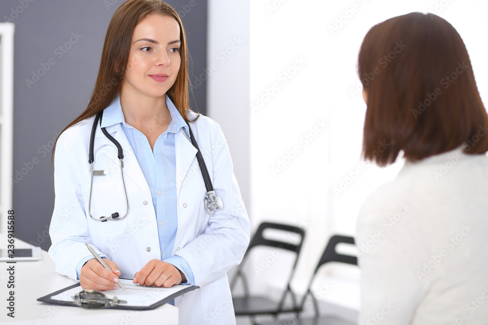 Doctor and patient discussing something while standing near reception desk in emergency hospital. Physician at work in clinic. Medicine and health care concept Doctor and patient discussing something while standing near reception desk in emergency hospital. Physician at work in clinic. Medicine and health care concept
