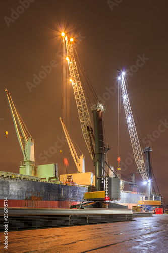 Night scene with cranes on illuminated quay loading a moored vessel, Port of Antwerp, Belgium.