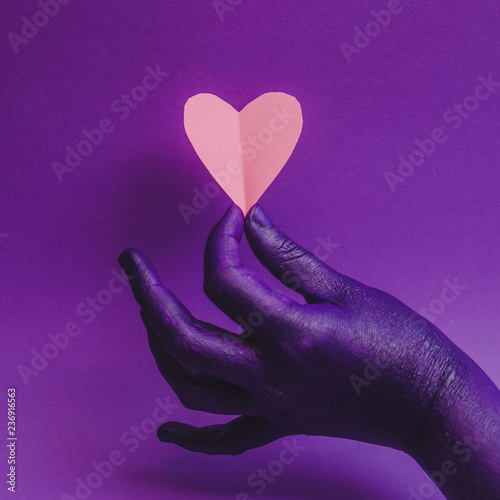 Female hand, showing beauty and skin care symbolism. Holding paper craft pink heart. fashion background, purple neon colors. Minimalism .