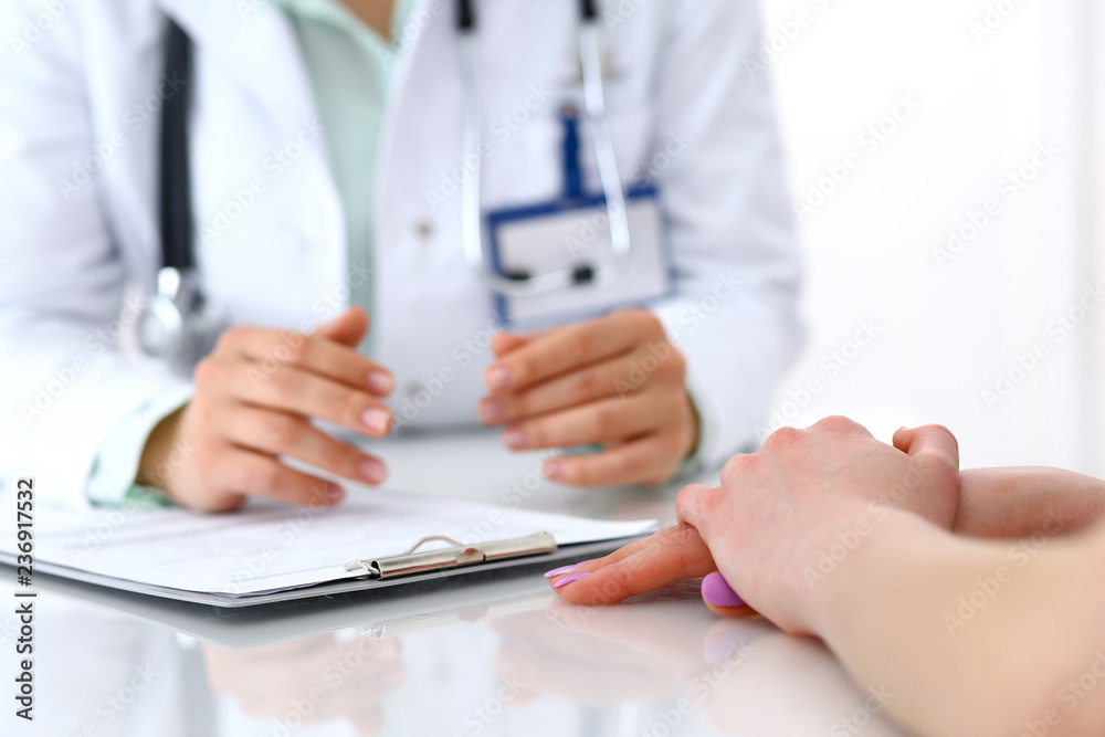 Doctor and patient talking while sitting at the desk in hospital office, close-up of human hands. Medicine and health care concept Doctor and patient talking while sitting at the desk in hospital office, close-up of human hands. Medicine and health care concept