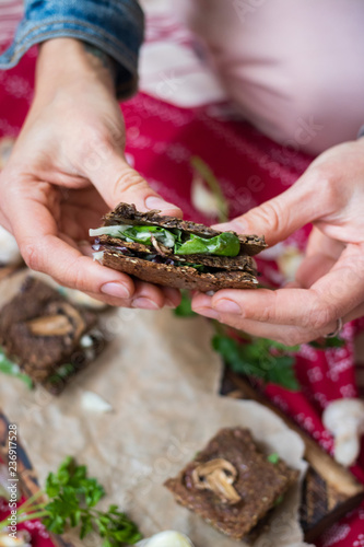 Crispy rye and flax seeds breads sandwich dehydrated and stuffed with fresh green salad leaves, mushrooms and hummus spread paste. Vegan, vegetarian snack on Christmas red tablecloth background. 