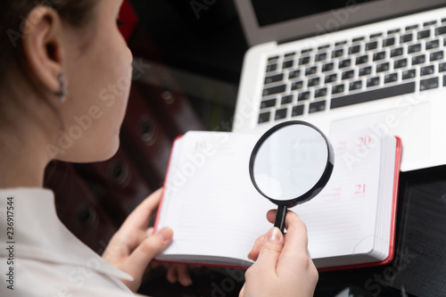 Young businesswoman with magnifying glass looking at diary on laptop background