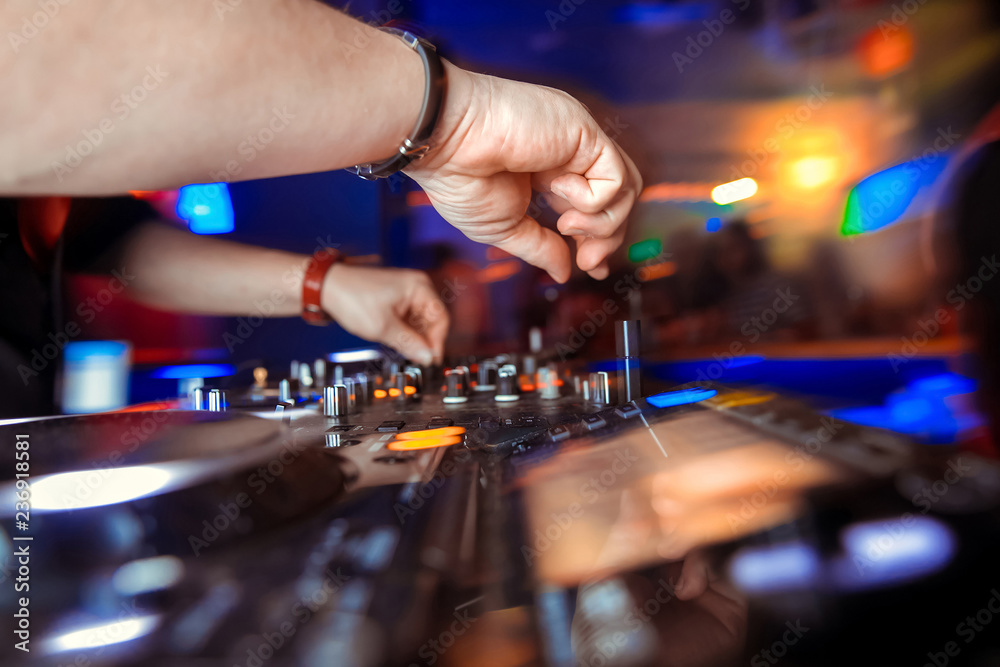 Dj mixes the track in the nightclub at party. Headphones in foreground and DJ hands in motion