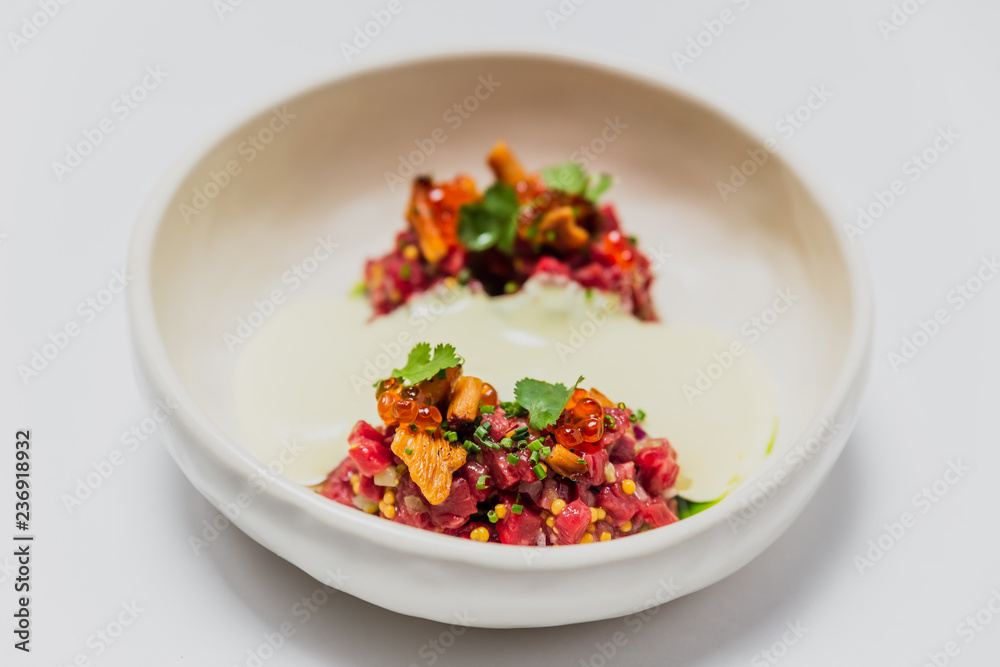 Meat tartare with mushrooms, sauce and greenery on a white plate Meat tartare with mushrooms, sauce and greenery on a white plate