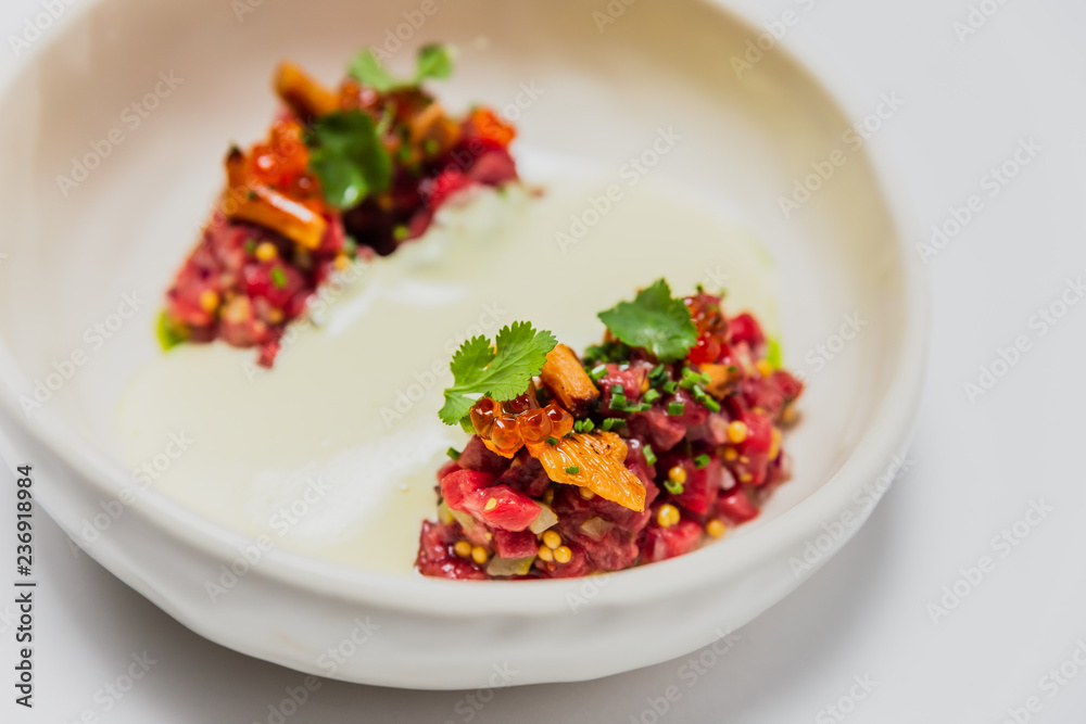 Meat tartare with mushrooms, sauce and greenery on a white plate Meat tartare with mushrooms, sauce and greenery on a white plate