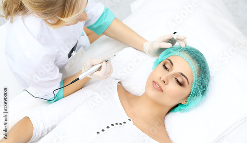 Professional beautician doing eyebrow tattoo at woman face. Permanent brow makeup in beauty salon  closeup.  Cosmetology treatment