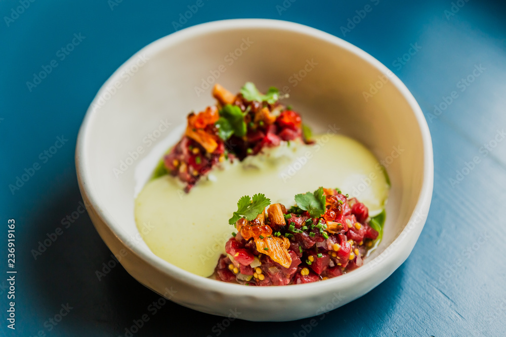 Meat tartare with mushrooms, sauce and greenery on a white plate Meat tartare with mushrooms, sauce and greenery on a white plate