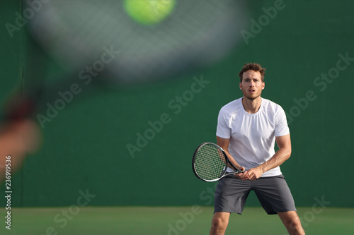 Tennis player focused on other player hitting ball with racket on court. Men sport athletes players playing tennis match together. Two professional tennis players on hard outdoor court during game. © Maridav