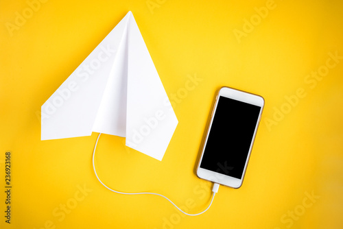 Mobile phone and paper airplane on yellow background. Travel concept. Speed Internet concept.