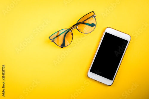 Mobile phone and glasses on yellow background photo