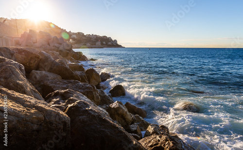 Moving wave and water of mediterranean sea touching rock beach making some splashing water in the air at sunrise.