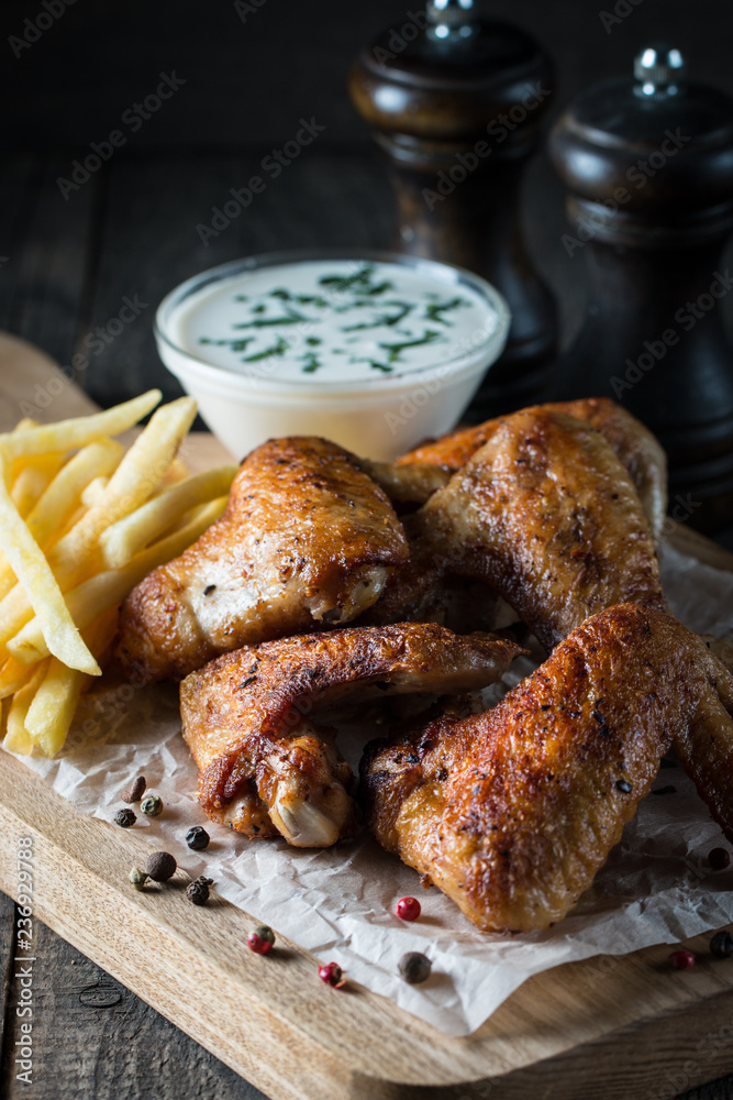 Barbecue grilled chicken wings close up with fries, tomato ketchup sauce and beer on wooden background. Meat food concept. Barbecue grilled chicken wings close up with fries, tomato ketchup sauce and beer on wooden background. Meat food concept.