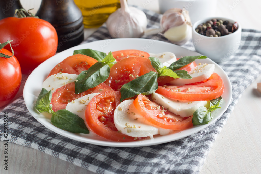 Photo of Caprese Salad with tomatoes, basil, mozzarella, olives and olive oil on wooden background. Italian traditional caprese salad ingredients. Mediterranean, organic and natural food concept.