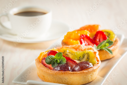 Photo of a fruit and berry tart dessert with toss sugar on wooden background. Fresh delicious sweet cake with raspberries, grapes, strawberries, cherry, kiwi, grapefruit and cream.