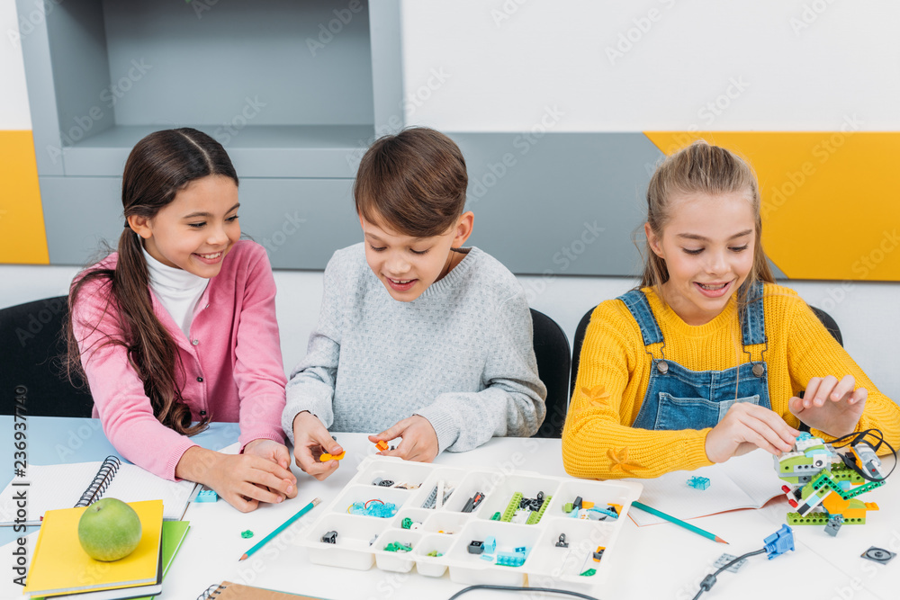 Fototapeta premium happy children sitting at desk and constructing robot in stem education class