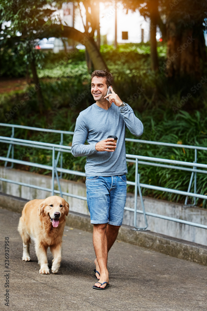 Guy on phone as he walks dog in park Guy on phone as he walks dog in park
