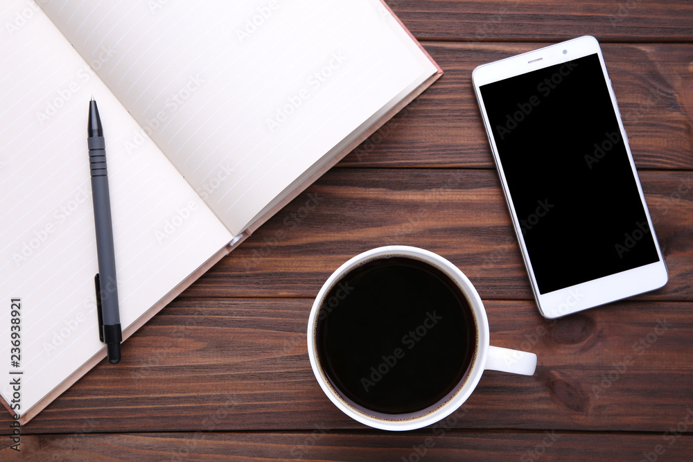Smart phone with notebook and cup of coffee on brown wooden background Smart phone with notebook and cup of coffee on brown wooden background